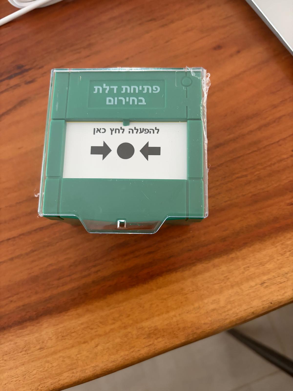 לחצן שחרור חירום ירוק עם מכסה שקוף והכיתוב פתיחת דלת בחירום