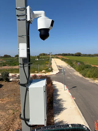 מצלמת PTZ לבנה וארון ציוד המותקנים על עמוד לצד דרך